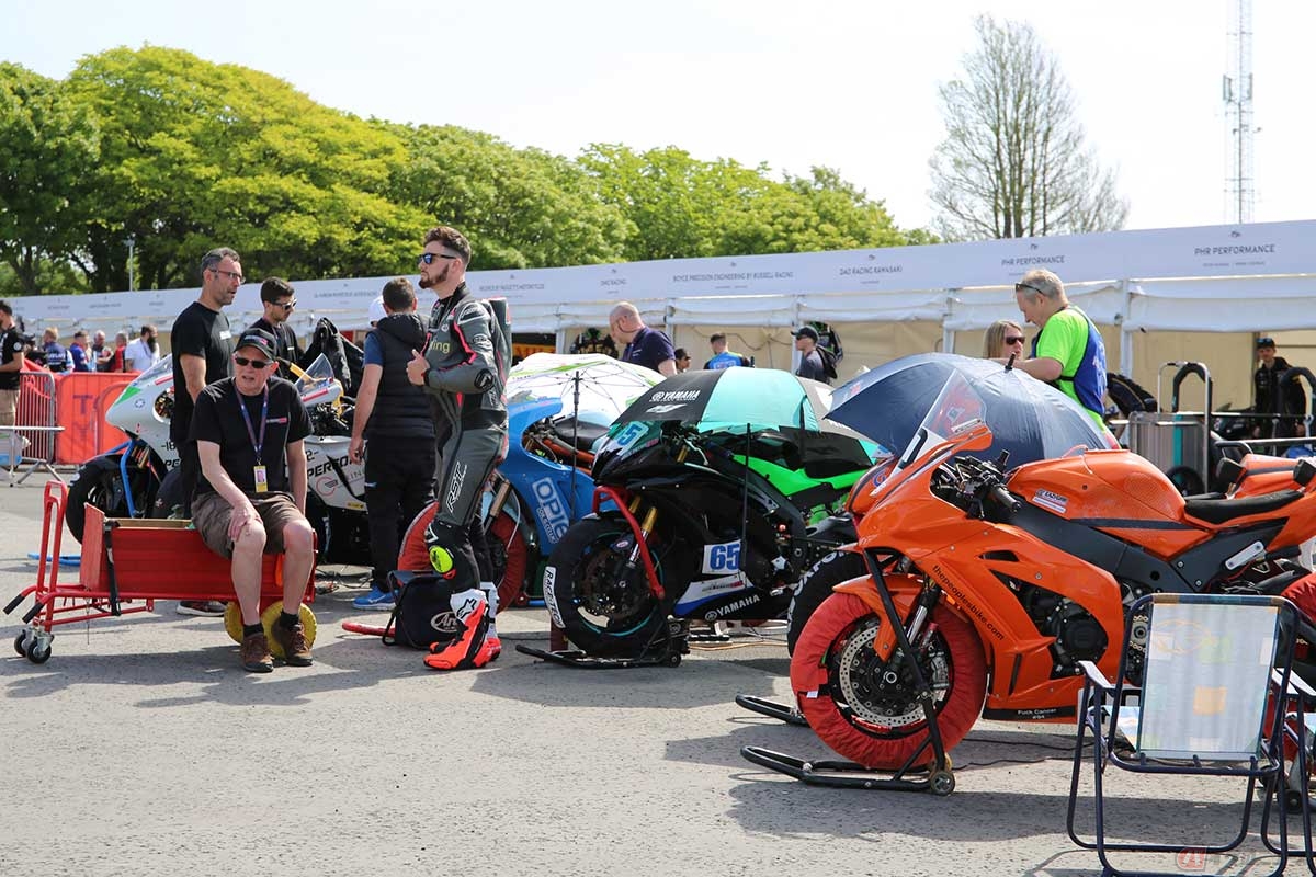 パドックで走行を待つマシンやライダーたち。奥の白い仮設テントは有力チームのためのもので、それ以外は写真のように屋根のない場所で待機する。このため、ガソリンが温まりすぎないよう傘をさしたりしている（写真／小林ゆき）