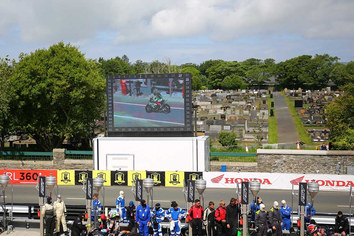 2022年のマン島TTレースでは、名物のスカウトの少年少女が運営していた手書きスコアボードが廃止され、仮設のビッグスクリーンでインターネット生配信の映像が流された。その向こう側はダグラス市営墓地（写真／小林ゆき）