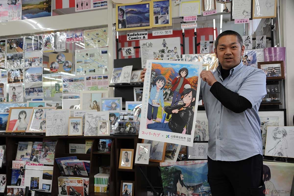 「北杜アニメツーリズム協議会」の会長も務める「スーパーおの」店長、小野桂一さん。掲げているのは2023年秋の「北杜市スタンプラリー」(10/14~11/12)完走記念のオリジナルポスター
