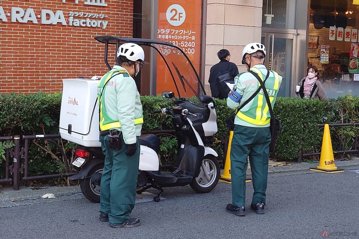 緑色の制服を着た駐車監視員が違法車両を厳しくチェックしている