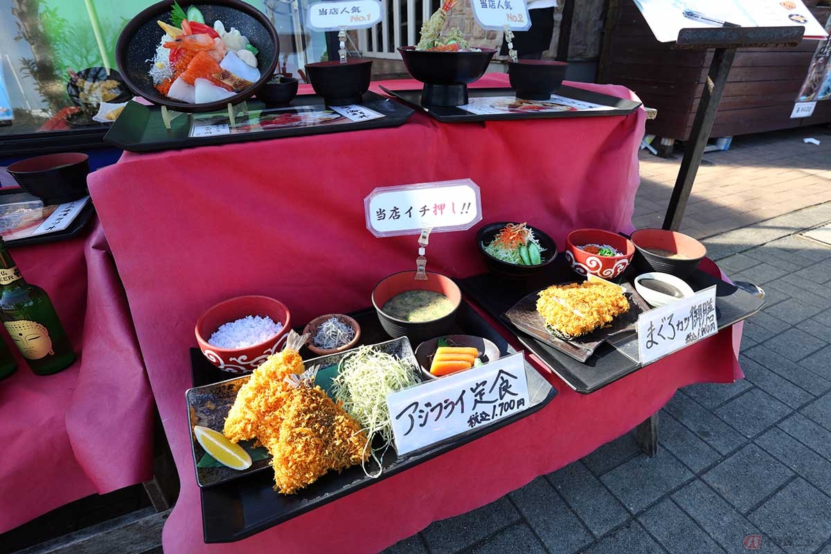 「座々丸（ざざまる）」の店頭に並ぶメニューのサンプル。足をとめて見ていく人が多い。「アジフライ定食」は「当店イチ押し!!」だった