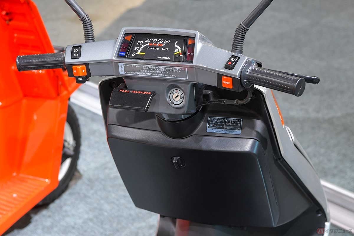 乗用車的なスピードメーター。手前のパーキングレバーをセットするとスイングジョイントと後輪軸を同時にロックし、自立するのでスタンドの必要がない。インナーレッグシールドにはグローブボックスも装備