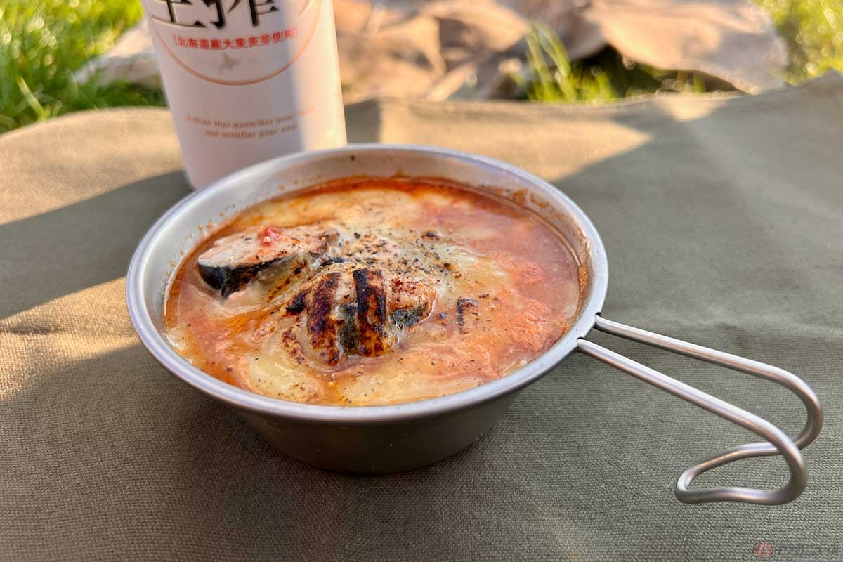 キャンプ飯の簡単アレンジレシピで完成した「炙りチーズのサバ缶トマトスープ」。チーズの焦げ目とトマト色のスープが食欲をそそる。ビールにもよく合う